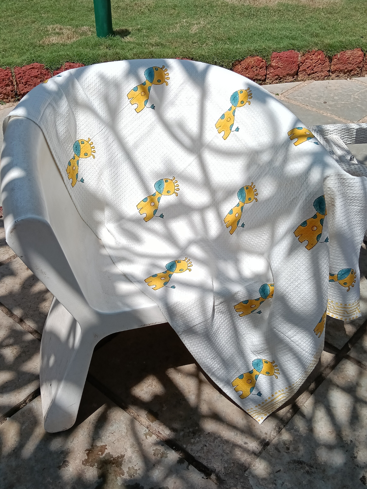 A white cotton bath towel with a hand block print design featuring giraffes in yellow and blue colors.