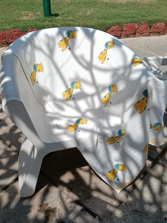A white cotton bath towel with a hand block print design featuring giraffes in yellow and blue colors.